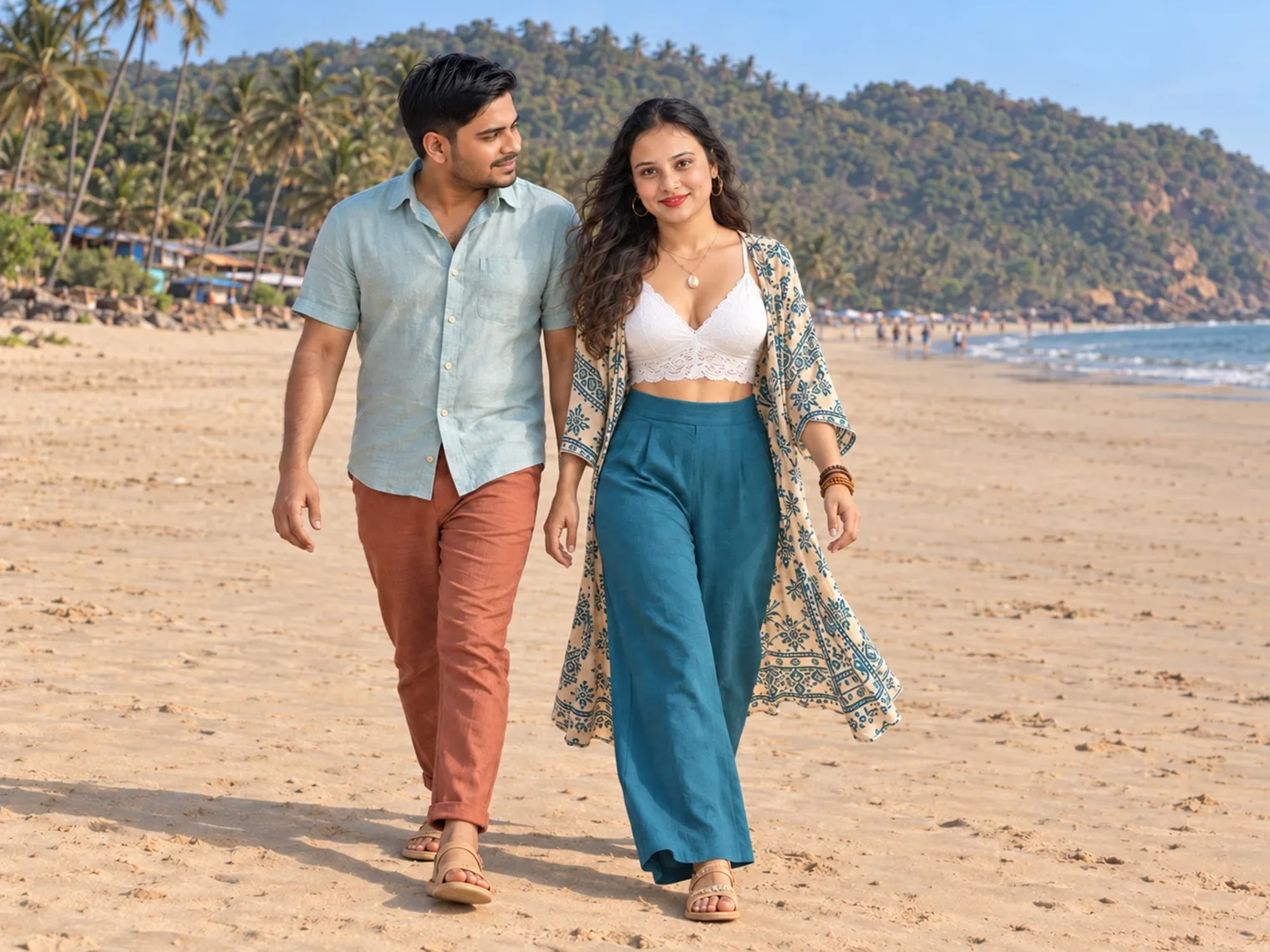 Nav and Vandana walking across a wide, nearly empty stretch of sand, a palm-covered hill and huts under the trees behind them.