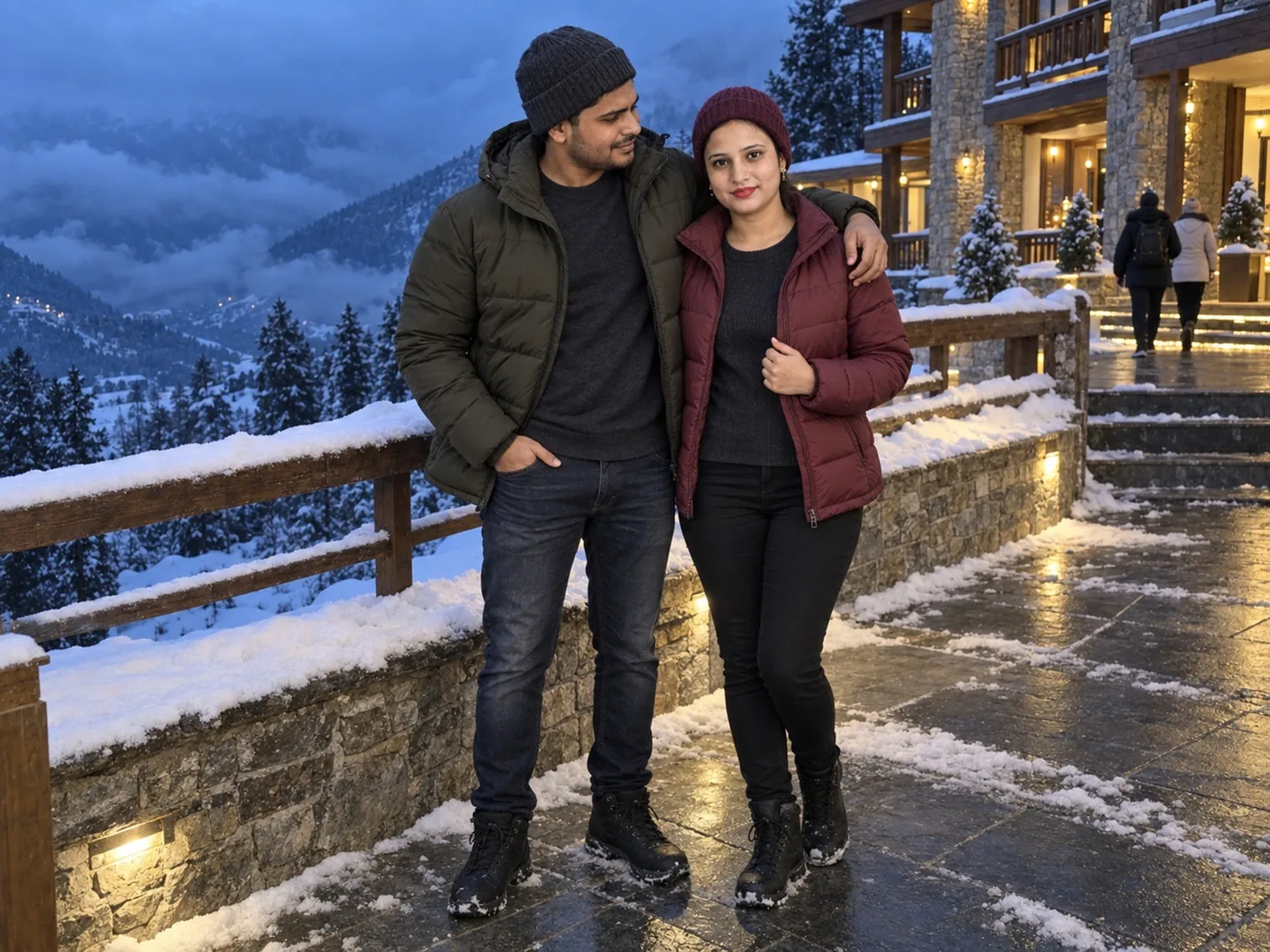 Nav and Vandana on a wet stone terrace at dusk, snow along the wall behind them and forested hills with cloud in the valley.