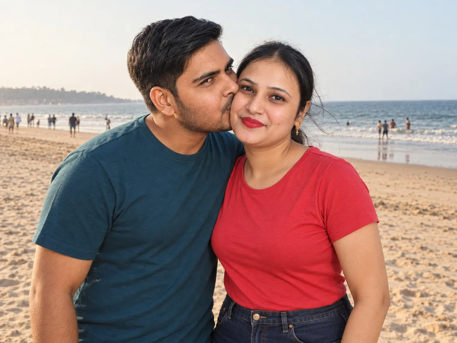 Nav kissing Vandana's cheek on Calangute beach, wide sand and people at the water's edge behind them.