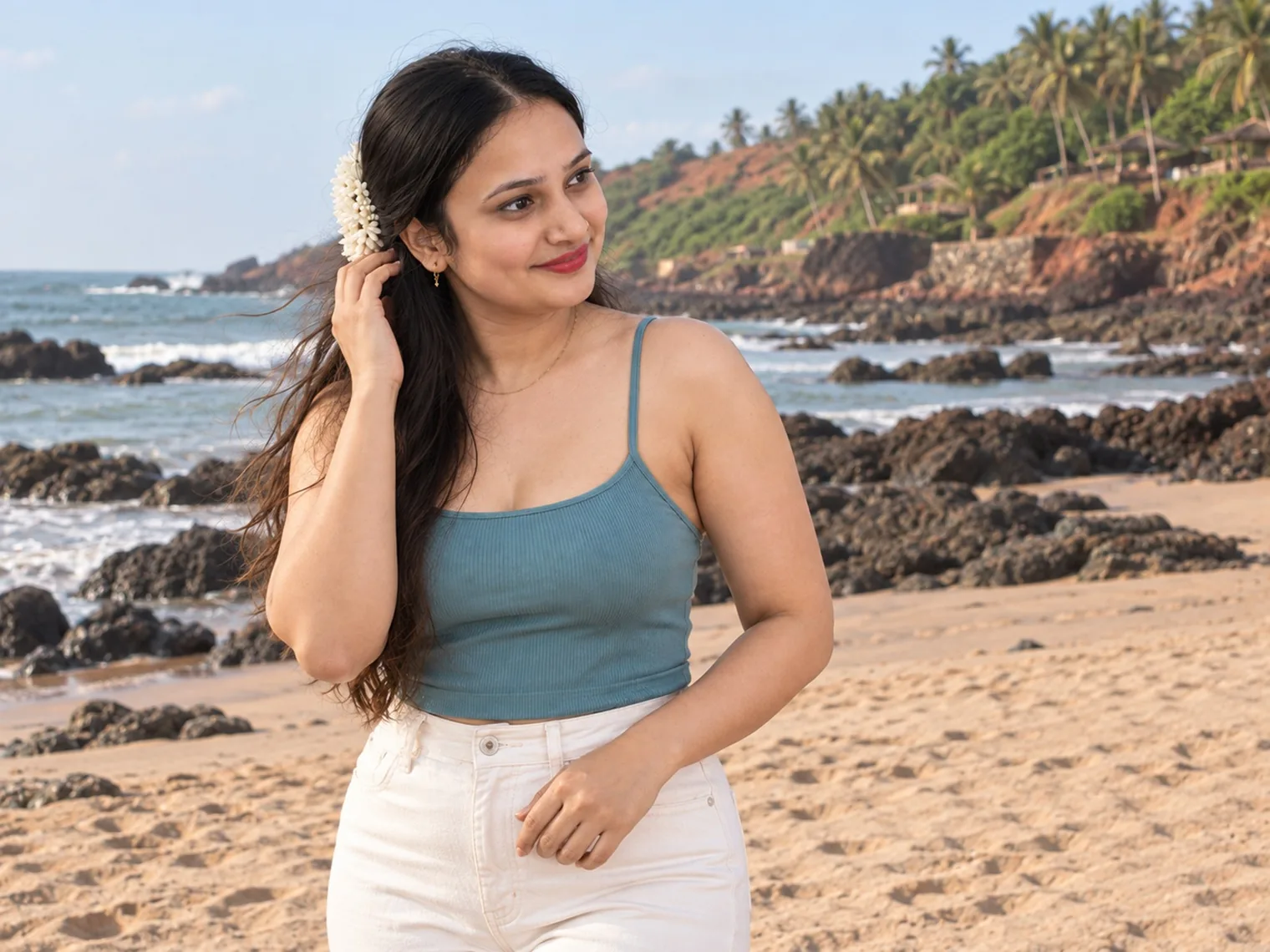 Vandana on Vagator beach, with black rocks at the water's edge and a green headland behind.