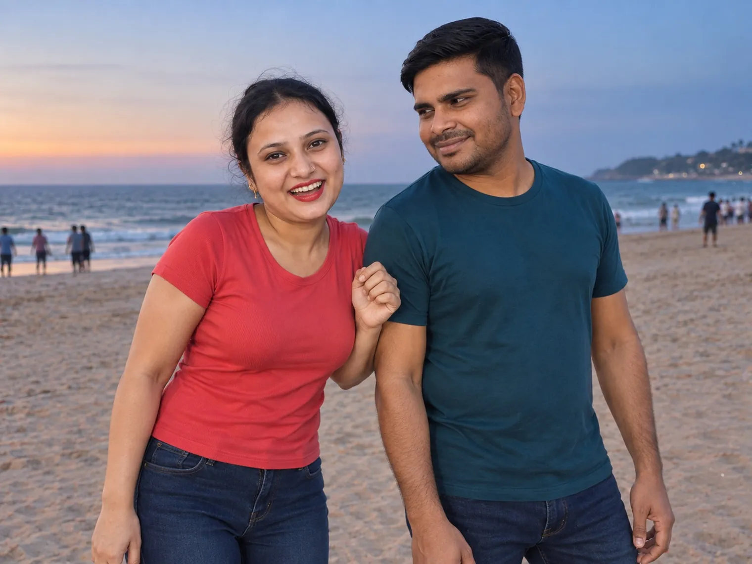 Vandana in a red T-shirt, smiling and holding Nav's arm, Nav beside her looking at her, on Calangute beach with people at the water's edge and an orange glow low in the sky.