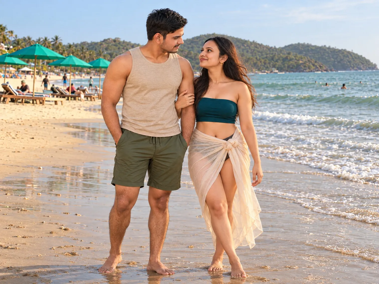 Nav and Vandana walking arm in arm on the wet sand at the water's edge in Palolem, green umbrellas and sunbeds along the beach and a wooded headland across the bay.